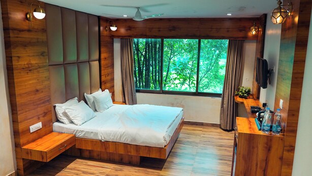 Un dormitorio moderno con cama de madera, un banco empotrado, televisor y un ventanal con vistas a árboles.