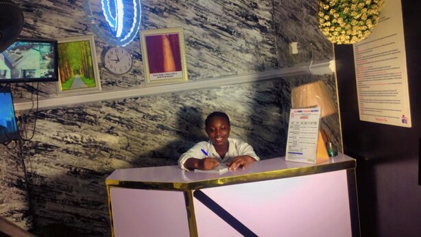 A reception desk with a marble wall background, a clock, framed pictures, and a bulletin board. - Autograph Apartment (Lagos)