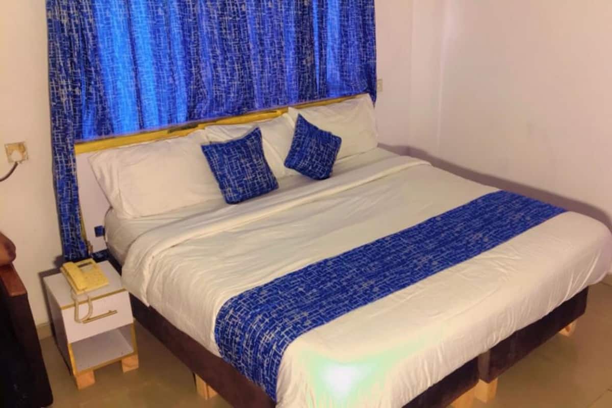 Ein Bett mit weiß-blauer Bettdecke, zwei blaue Kissen und einem hölzernen Kopfteil.