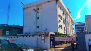 A building with a sign for 'Ikeja Budget Hotel' and a pharmacy sign on the side. - Autograph Apartment (Lagos)
