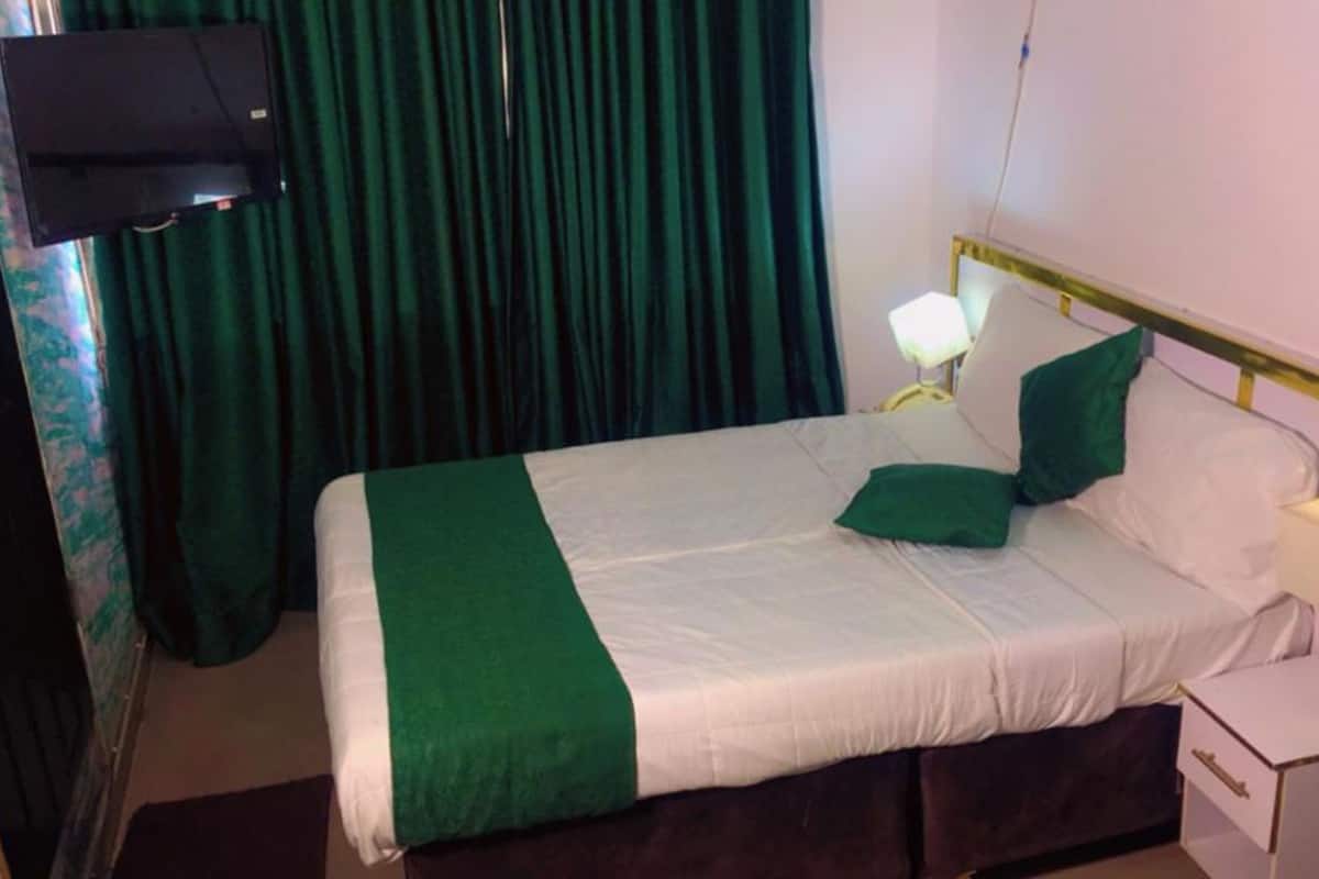 Ein Hotelzimmer mit Bett, Nachttisch, Lampe und einem an der Wand montierten Fernseher.