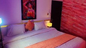 A hotel room with a bed, pillows, a nightstand with a lamp, a painting on the wall, and a door. - Autograph Apartment (Lagos)