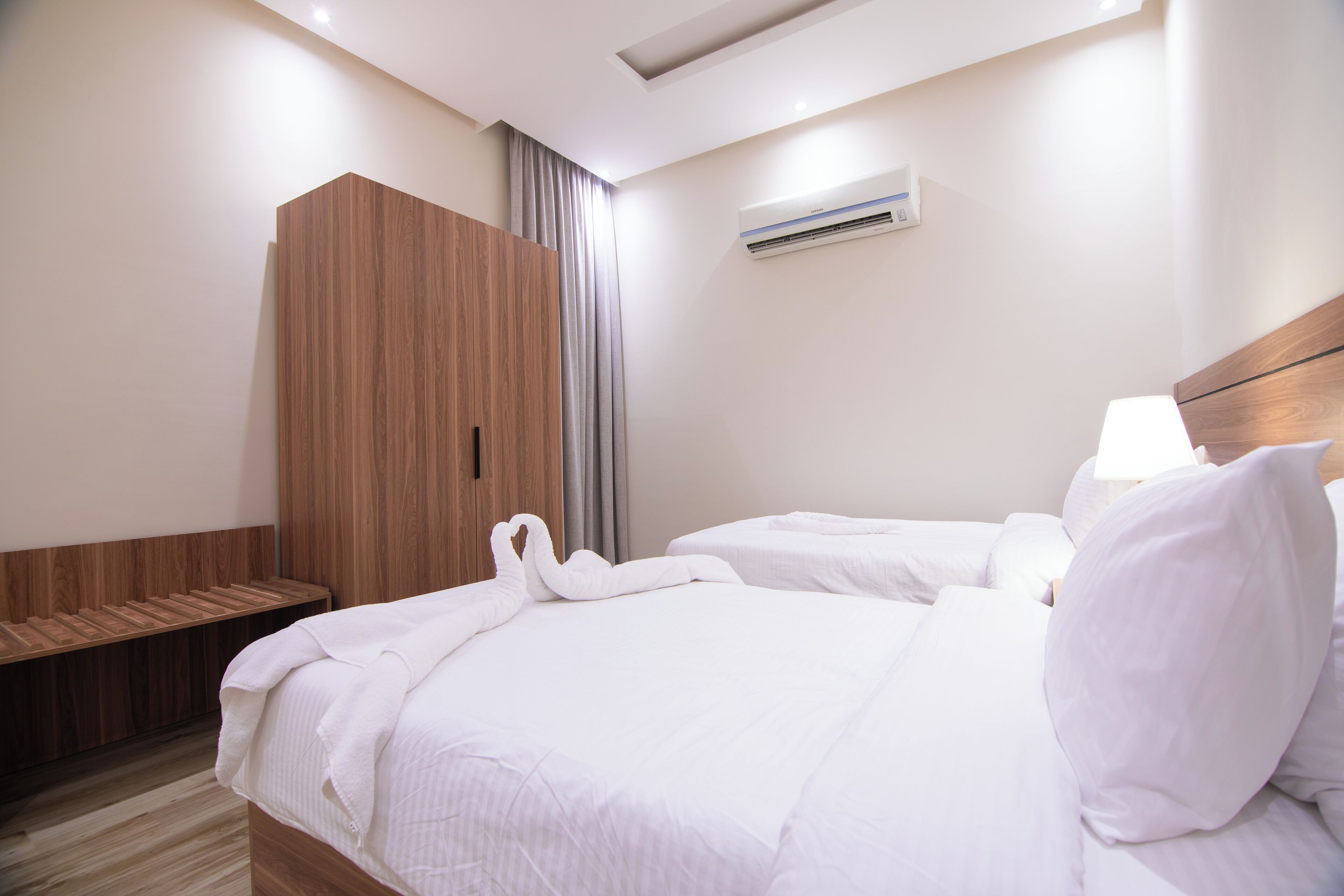A hotel room with a wooden wardrobe, a bed with white bedding, and an air conditioning unit on the wall.