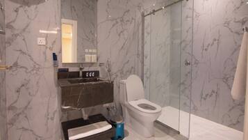 A modern bathroom with a marble wall, a glass shower enclosure, a white toilet, and a built-in sink.