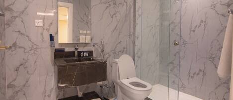 Un baño moderno con pared de mármol, cabina de ducha de vidrio, inodoro blanco y lavamanos empotrado.