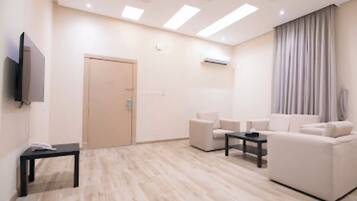 Un salon moderne comprenant un ensemble de canapés, une table basse, un téléviseur à écran plat fixé au mur et une porte donnant sur une autre pièce.