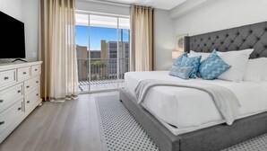 Ein Schlafzimmer mit einem großen Bett, einem Fernseher auf einer Kommode und einem Balkon mit Vorhängen.
