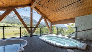 Una terraza de madera con dos jacuzzis y vistas a las montañas.