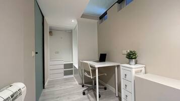 Una habitación moderna y estrecha con un escritorio, una silla, un radiador y una pequeña planta en maceta.