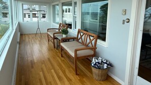 A covered porch with wooden flooring, a bench, two chairs, and a small table with a plant. - The Sunset Lighthouse Marblehead - Exclusive Waterfront 3brm/2.5bath Home (Marblehead)