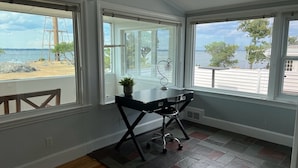 A room with a desk and chair, large windows with a view of the beach and ocean, and a potted plant on the desk. - The Sunset Lighthouse Marblehead - Exclusive Waterfront 3brm/2.5bath Home (Marblehead)