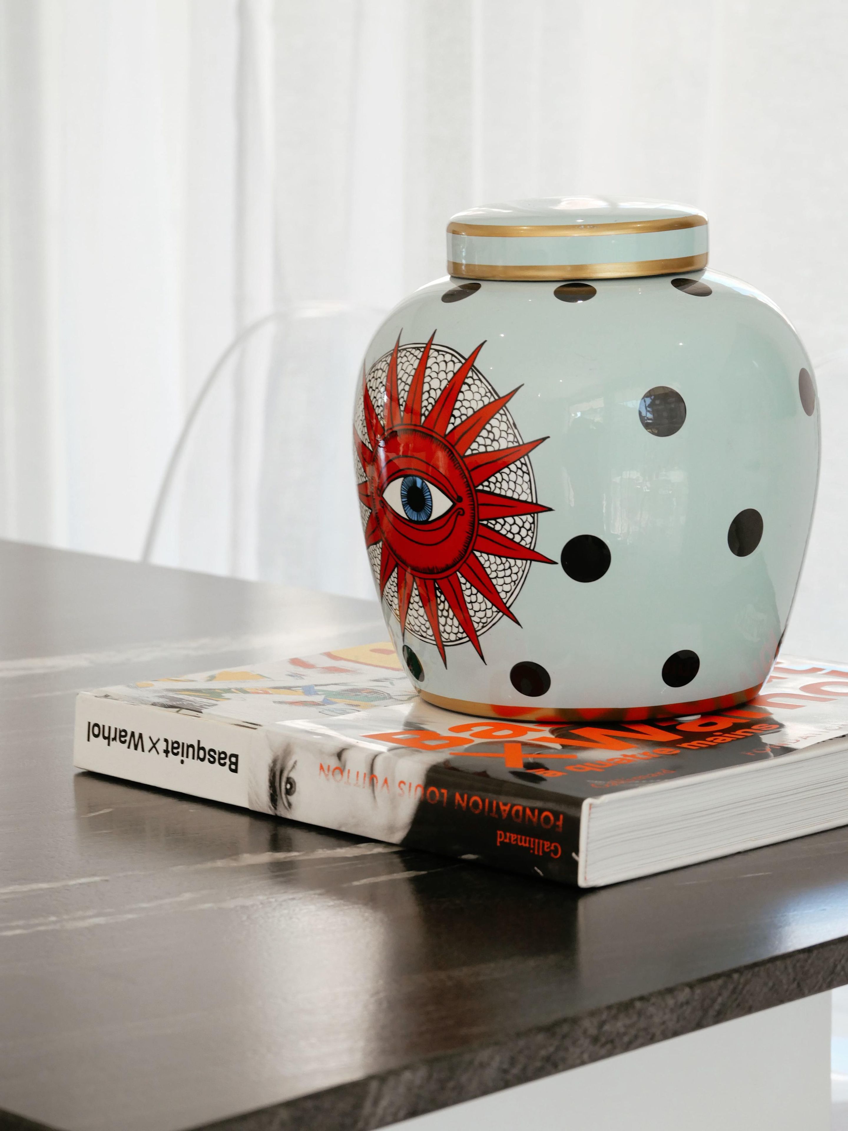 Un jarrón de cerámica con un diseño de sol sobre una mesa, junto a un libro.