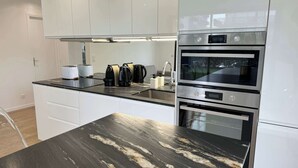 A modern kitchen with white cabinets, a black marble countertop, and stainless steel appliances including an oven and a microwave. - Jardin privé + parking · 6 pers · plage 2 min (Deauville)