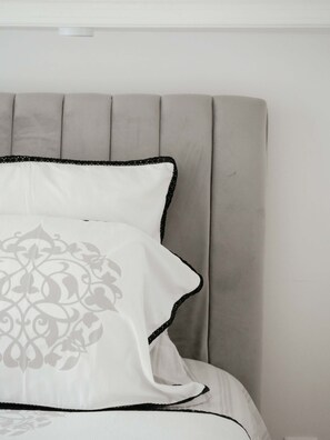 A bed with a grey upholstered headboard and white bedding with black trim and a grey floral pattern.