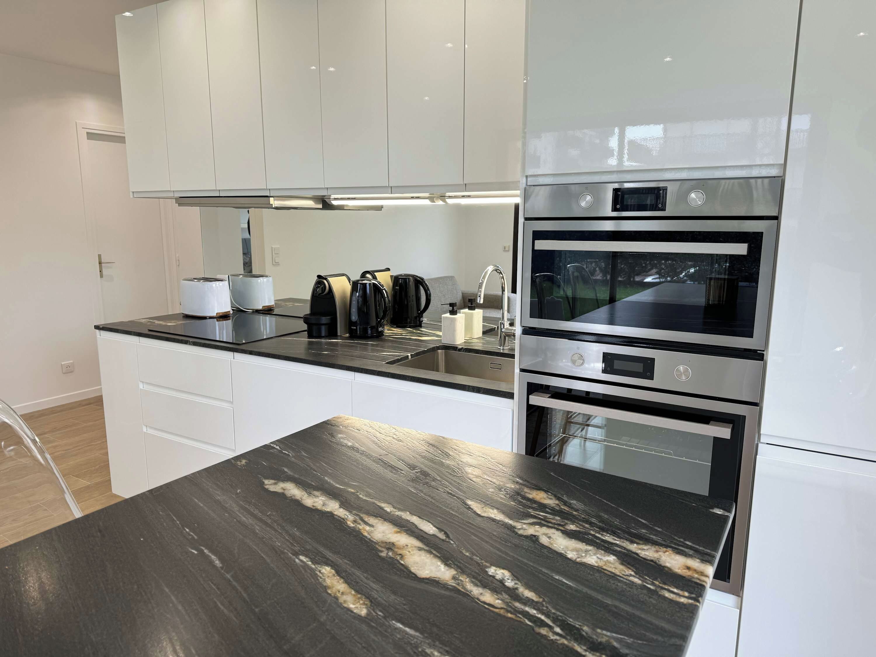 A modern kitchen with white cabinets, a black marble countertop, and stainless steel appliances including an oven and a microwave.