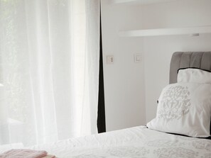 A bedroom with a bed, white curtains, and a headboard.
