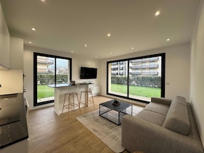 Eine moderne Wohnung mit Küche, Essbereich und Wohnzimmer. Sie verfügt über große Fenster, einen Flachbildfernseher und ein Sofa.