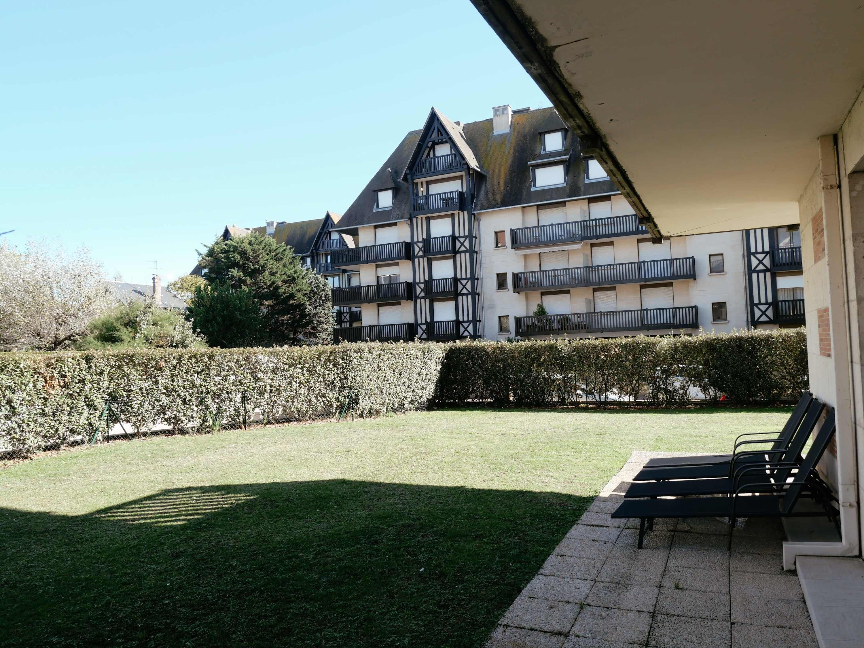 Une cour avec une pelouse, une haie et une rangée de fauteuils de jardin noirs.