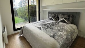 A bedroom with a large bed, a sliding glass door to a balcony, and built-in cabinets above the bed. - Jardin privé + parking · 6 pers · plage 2 min (Deauville)