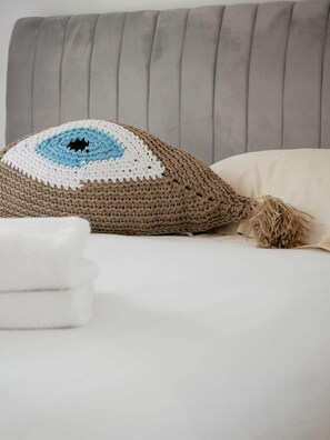 A bed with a grey upholstered headboard, a crocheted pillow with a blue and white pattern, and a white pillow.