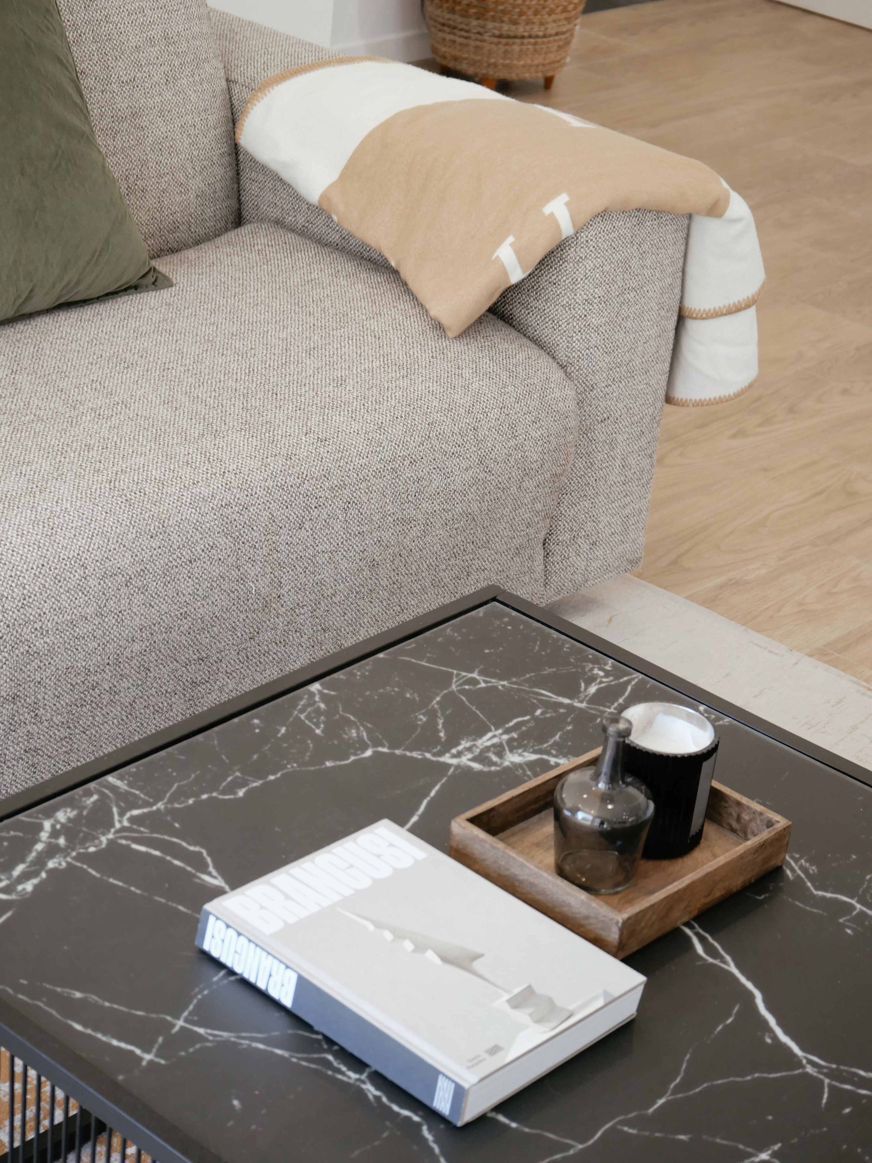 Un salon moderne avec un canapé gris, une table basse sur laquelle se trouvent un livre et un plateau, et une table d’appoint en bois.