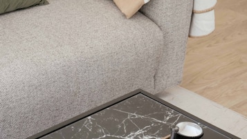 Un salon moderne avec un canapé gris, une table basse sur laquelle se trouvent un livre et un plateau, et une table d’appoint en bois.