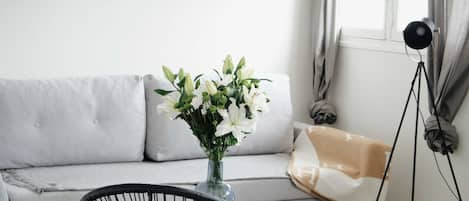 A modern living room with a grey sofa, a black wicker chair, a small table with a book, and a vase of flowers.