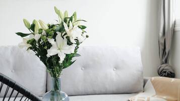 Un salon moderne avec un canapé gris, un fauteuil noir, un vase en verre contenant des fleurs blanches et un tableau encadré accroché au mur.