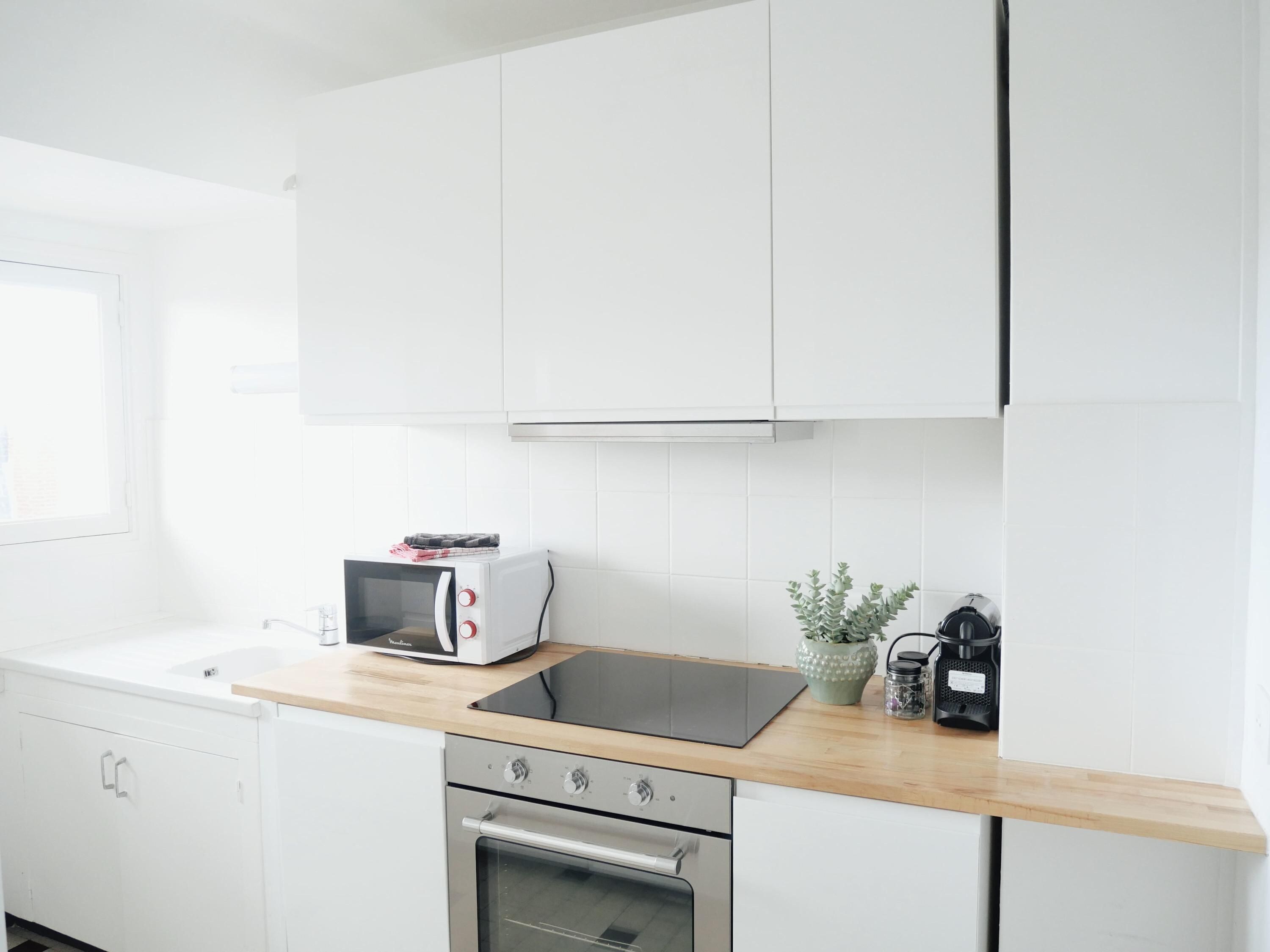 A modern kitchen with white cabinetry, a built-in microwave, a stove, and a wooden countertop.