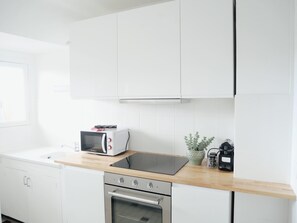 A modern kitchen with white cabinetry, a built-in microwave, a stove, and a wooden countertop. - Cœur de Deauville · vue sur les toits · 4 pers (Deauville)
