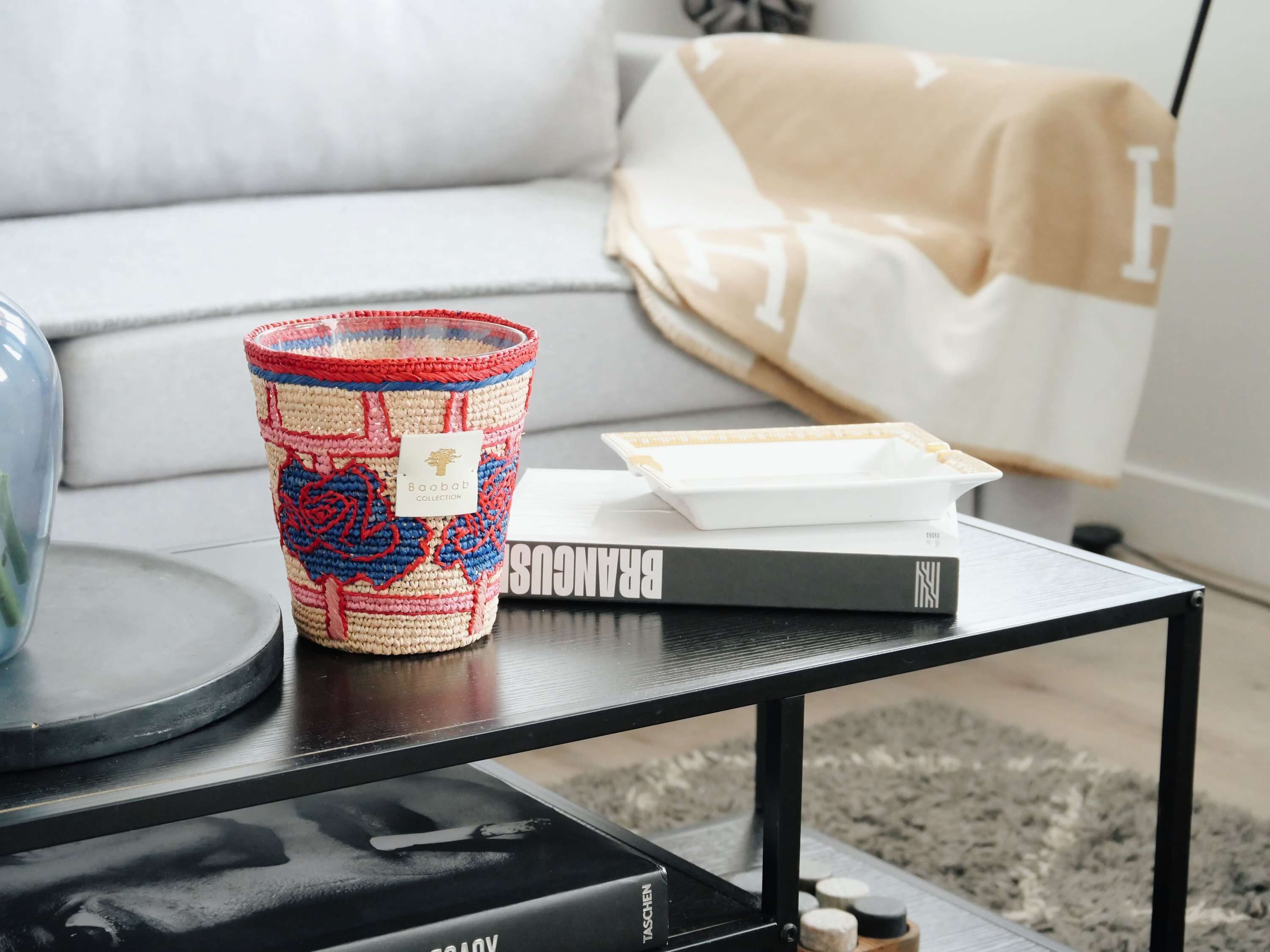 Ein Wohnzimmer mit einem schwarzen Couchtisch, einem gehäkelten Korb, einem Buch und einer weißen Ablagefläche.