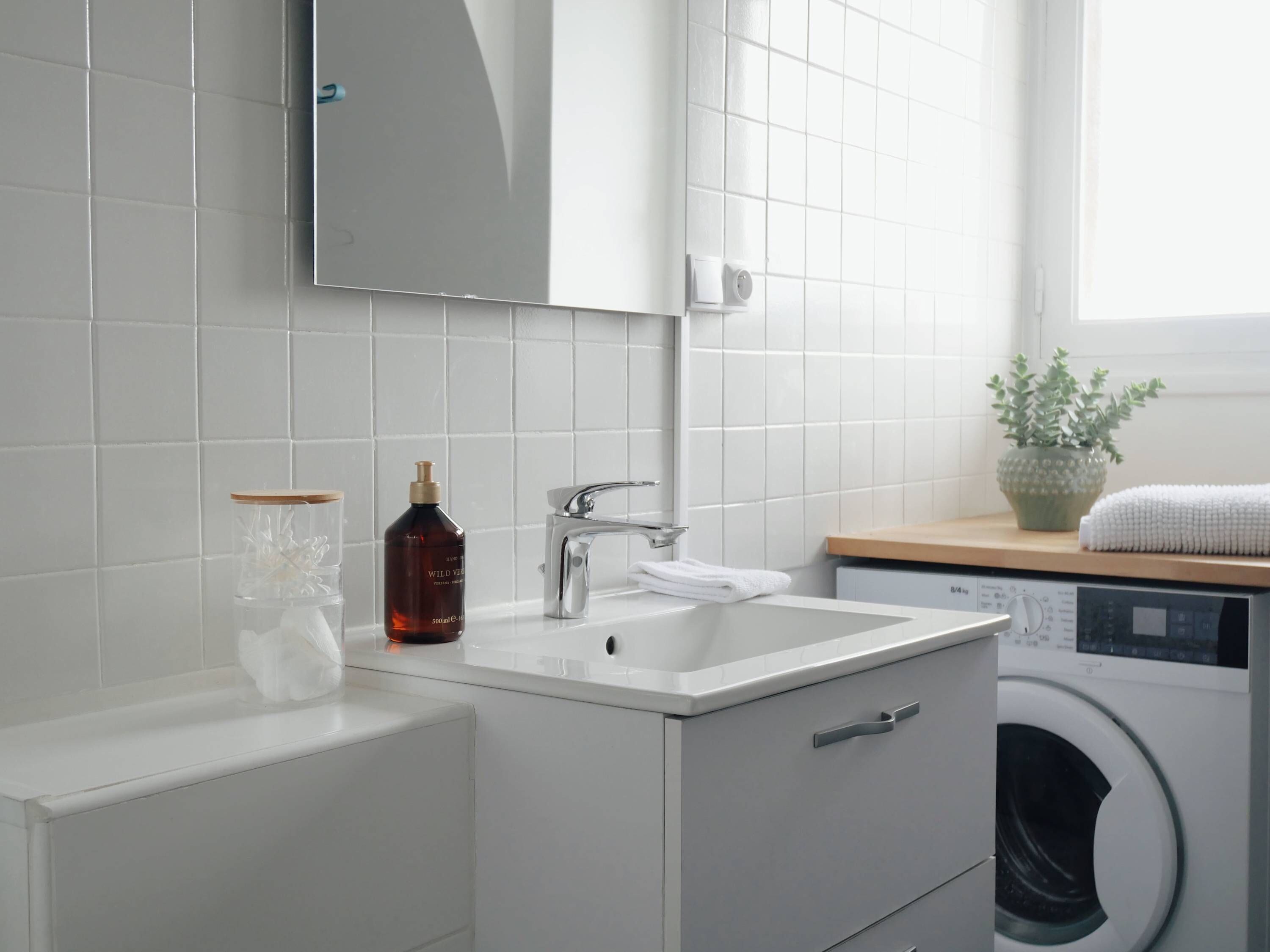 Ein modernes Badezimmer mit Waschbecken, Spiegel und integriertem Waschmaschinenanschluss.