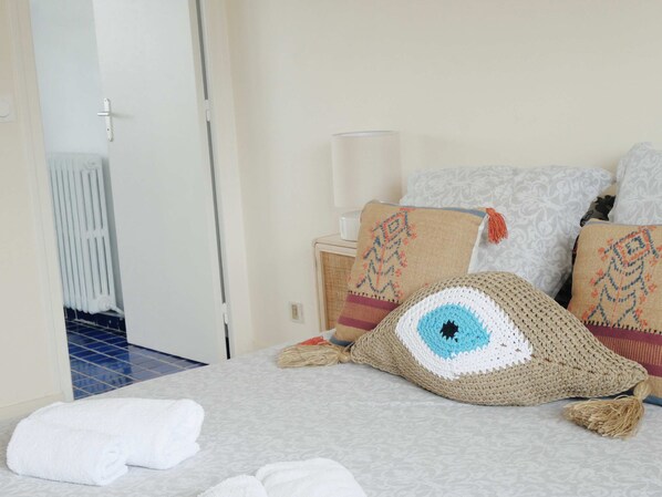 Una cama bien tendida con un edredón blanco, un cojín de ganchillo con un diseño azul y blanco, y una toalla blanca.