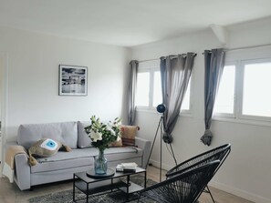 Una sala de estar moderna con un sofá gris, una mesita de centro, un sillón negro, una lámpara de pie y un cuadro enmarcado en la pared.