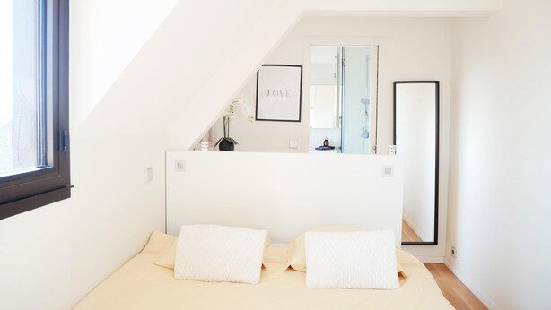 Ein modernes Schlafzimmer mit einem großen Bett, einem Nachttisch, einem Spiegel und einem gerahmten Bild an der Wand.