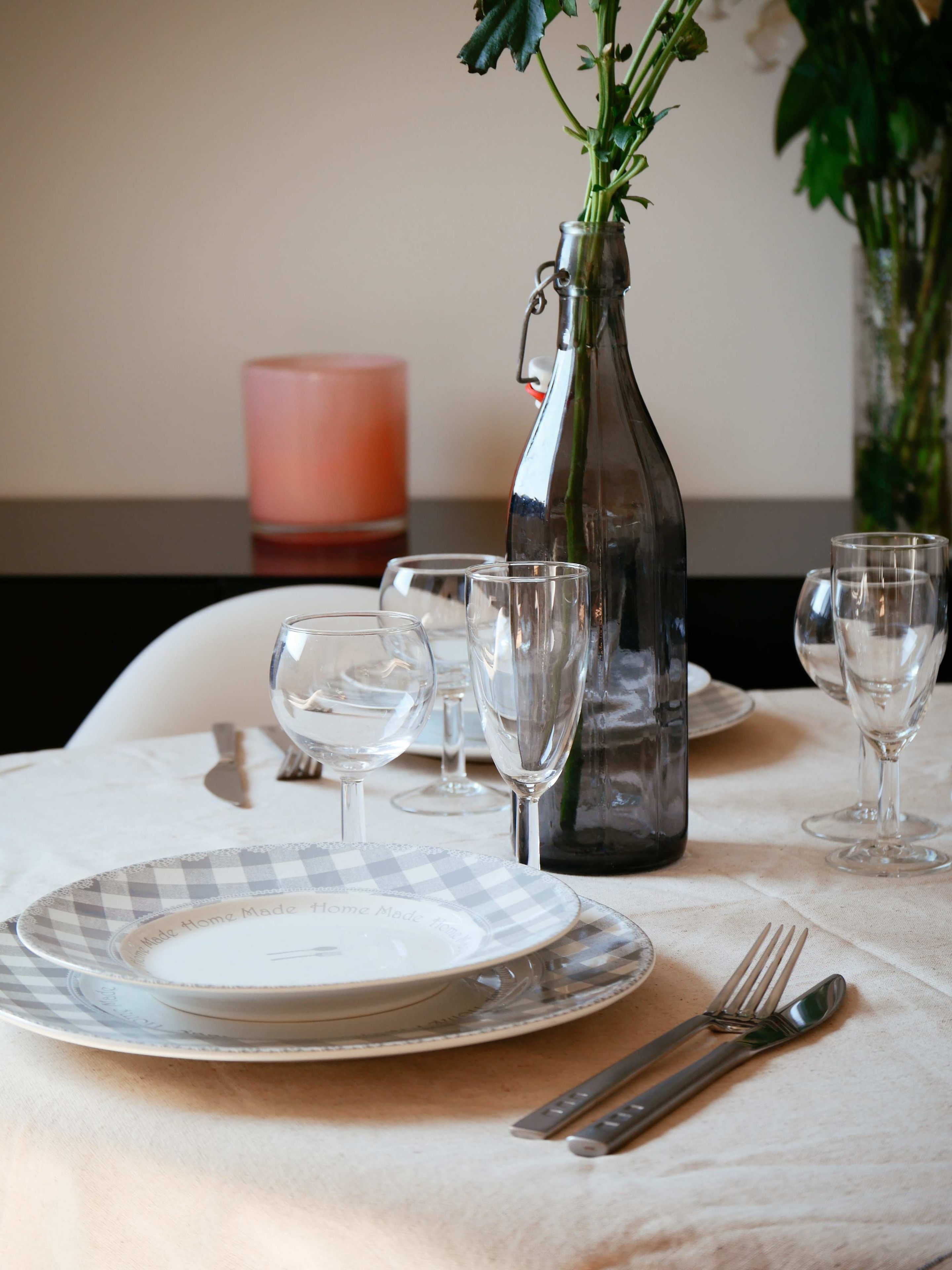 A table set with plates, glasses, cutlery, and a vase with flowers.