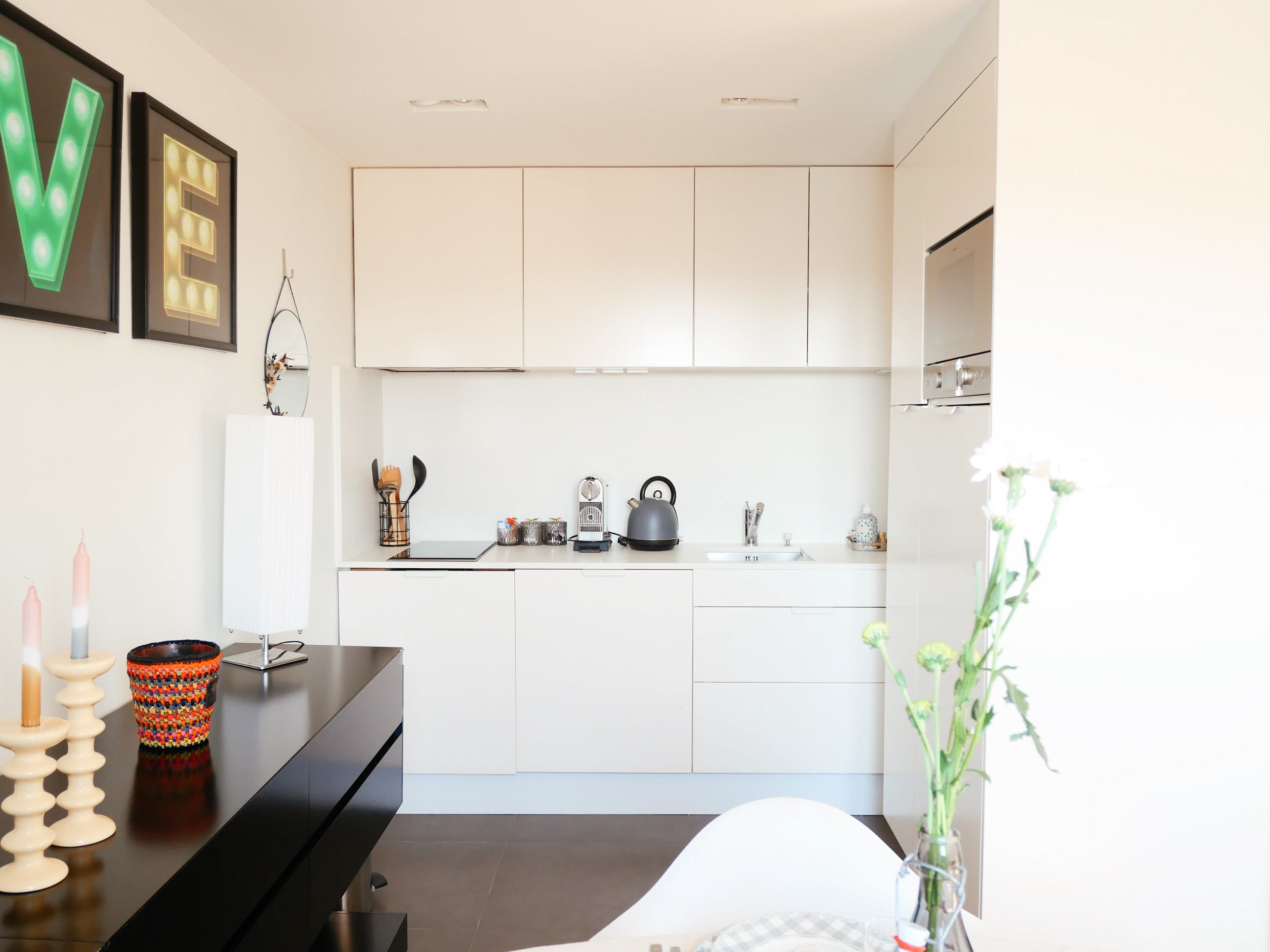 A modern kitchen with white cabinets, a black countertop, and a sink. There are decorative items like candles and a vase with flowers on the counter.
