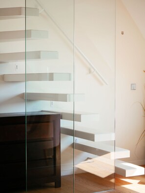Una escalera moderna con barandas de cristal, un banco de madera oscura y una pequeña planta a la derecha.