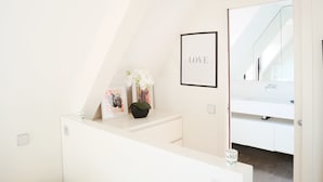 Ein modernes, minimalistisches Badezimmer mit einem weißen Waschbecken, einem gerahmten 'LOVE'-Schild und einem kleinen Blumentopf.