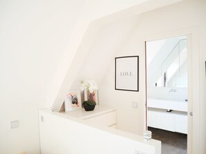 Et moderne, minimalistisk badeværelse med en hvid vask, et indramet 'LOVE'-skilt og en lille potteplante.