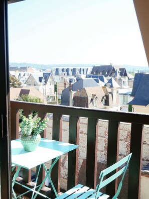 En balkon med et bord og stole, en potteplante og udsigt til boligbygninger.