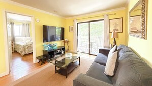Un salon avec un canapé, une table basse, un téléviseur et un balcon équipé d’une chaise.