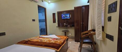 A hotel room with a bed, a desk, a chair, a TV, and a bathroom visible through an open door.