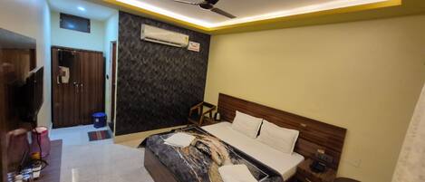 A modern hotel room with a bed, bedside table, nightstand, and a ceiling fan.