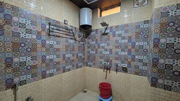 A bathroom with patterned tiles, a shower, a red bucket on a stool, and a towel rack.
