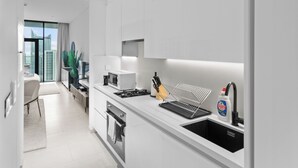A modern kitchen with white cabinetry, a microwave, a stove, and a sink. - Waves - Chic High-Floor Studio Retreat with Canal Views (Dubai)
