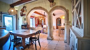 A spacious dining area with a wooden table and chairs, stone pillars, and a view into another room. - Mas Suéjol Gîtes, Gîtes du Mas Suéjol en Cévennes (Anduze)