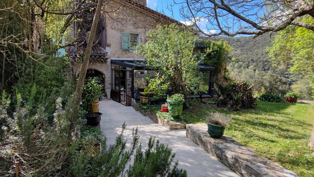 A rustic stone building with a covered patio, surrounded by lush greenery and a stone pathway leading to an entrance. - Mas Suéjol Gîtes, Gîtes du Mas Suéjol en Cévennes (Anduze)