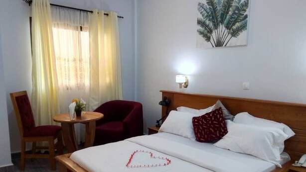 Habitación de hotel con cama, una silla, una mesita, una lámpara y un cuadro en la pared.