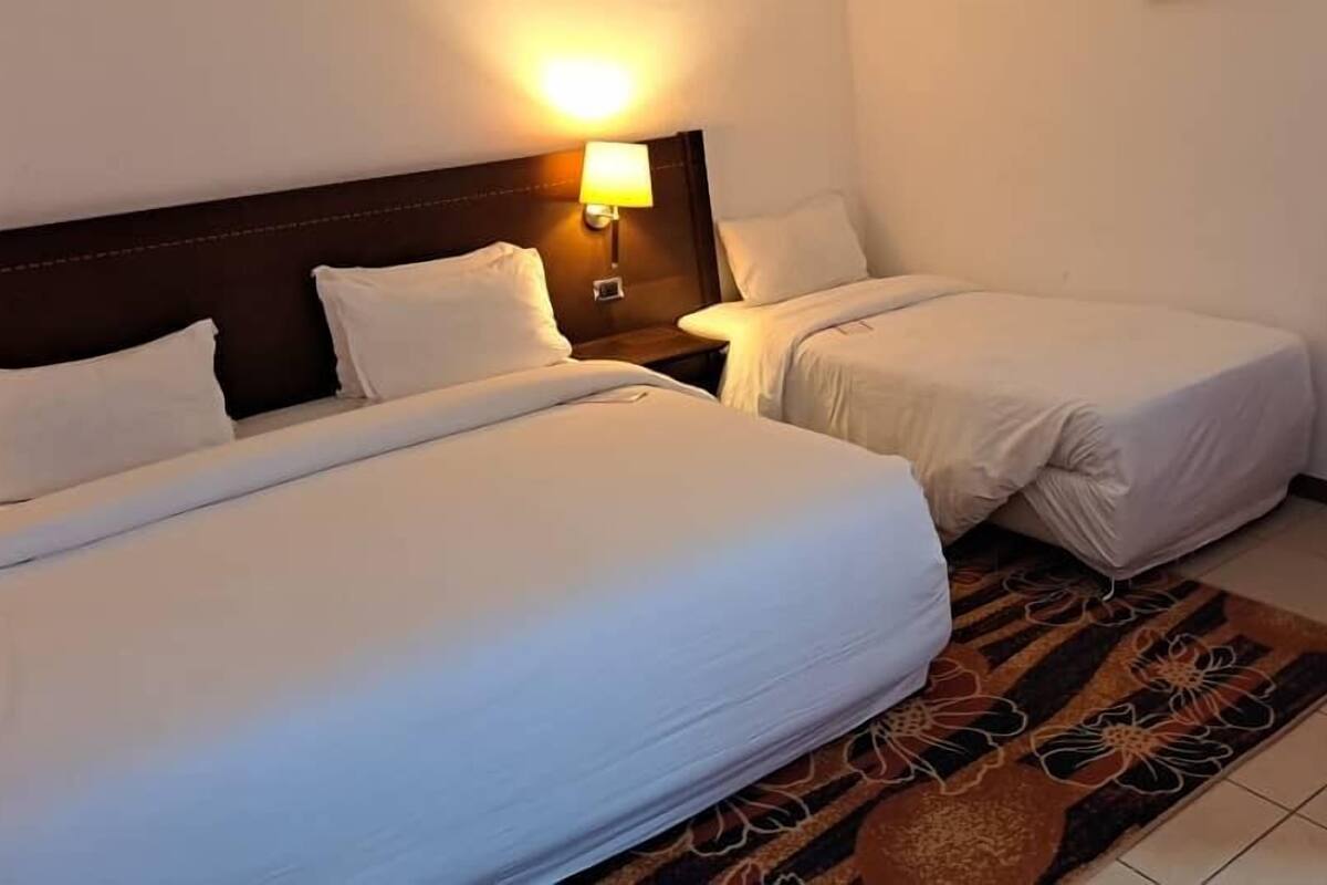Ein Hotelzimmer mit zwei Einzelbetten, einem Nachttisch mit Lampe und einem gemusterten Teppich.